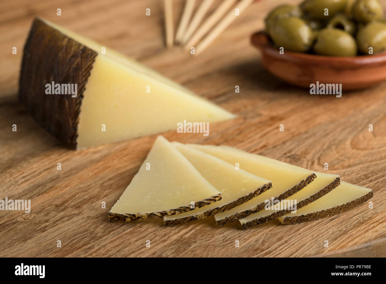 Rebanadas de queso Manchego tradicional española y aceitunas en el fondo Foto de stock
