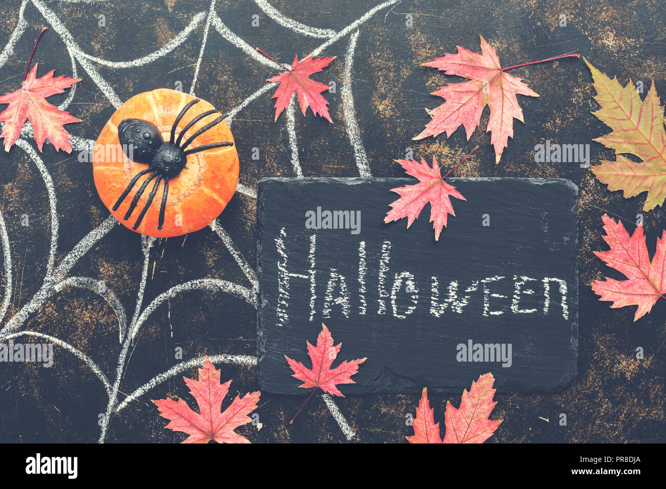 Halloween, la calabaza, la araña roja, hojas de arce, tela de araña dibujado con tiza en un oscuro fondo rústico. Cartel con texto-Halloween. Vista superior,flat Foto de stock