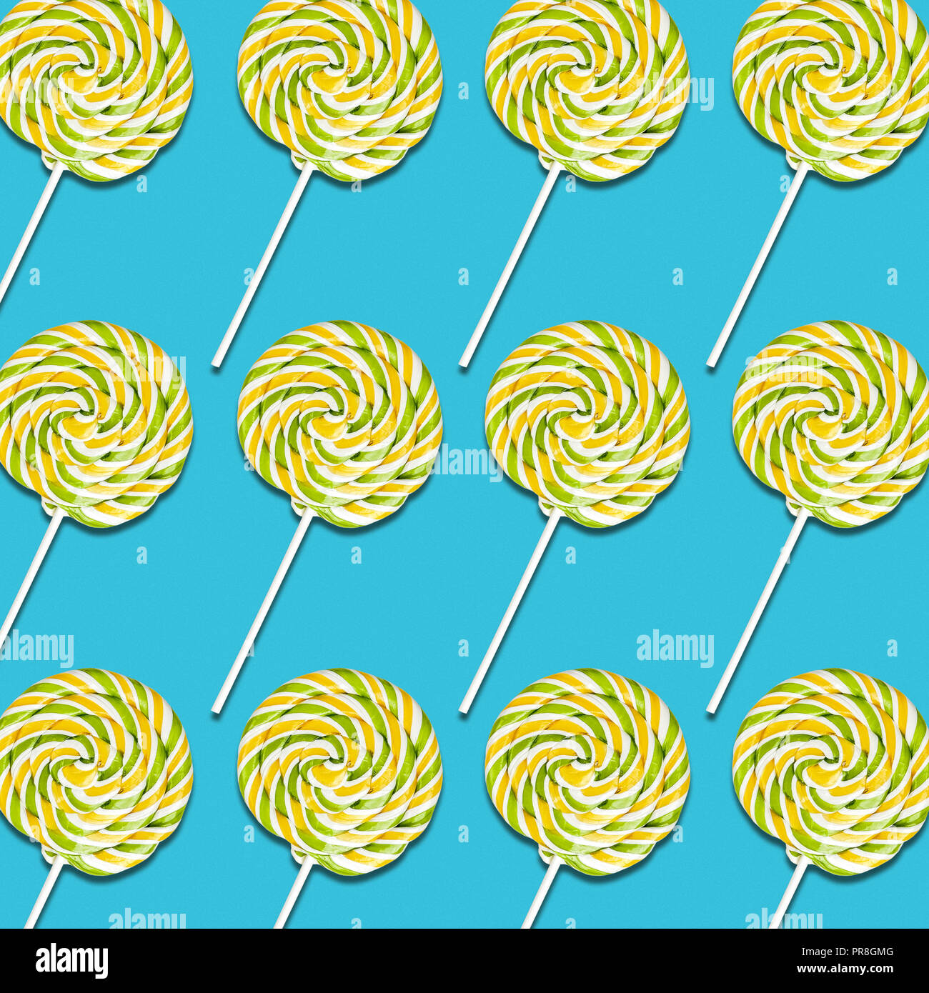 Disposición simétrica de amarillo y verde de lollipop caramelos sobre fondo turquesa, coloridos dulces de textura de alimentos Foto de stock