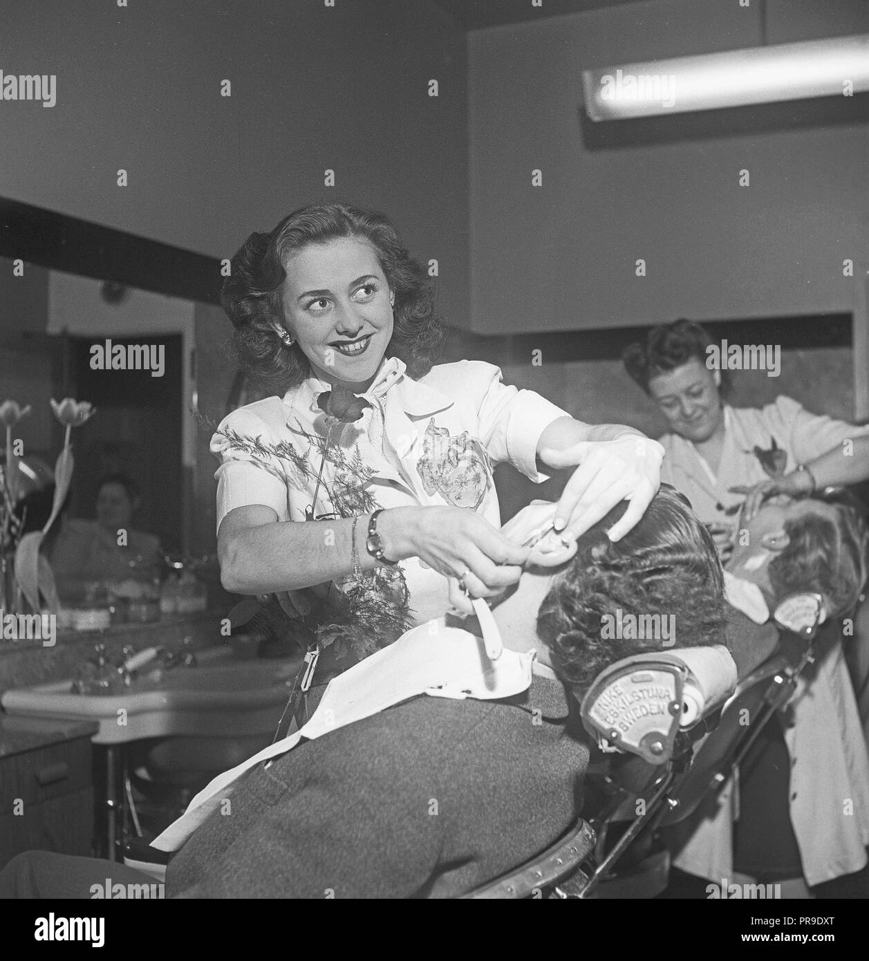 Obtener un afeitado en la década de 1940. Una joven es un hombre afeitado en la barbería. Ella usa una maquinilla de afeitar y recta es retratada aquí mientras afeitado cuidadosamente cerca de la oreja del hombre. Suecia 1940. Foto Kristoffersson ref un48-1 Foto de stock