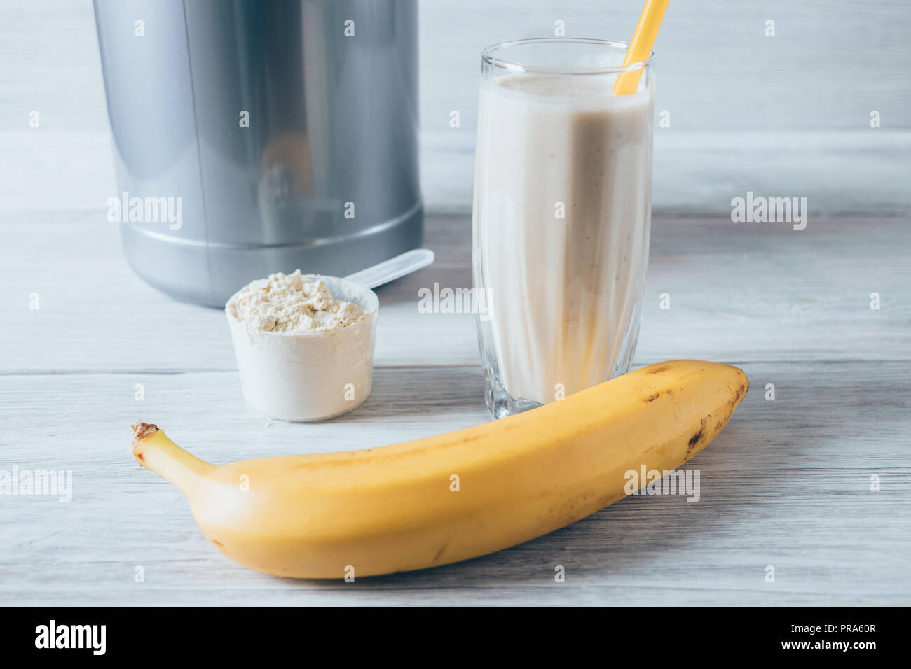 Vaso de batido de proteína de suero de leche junto a la boca de medición de  polvo y banana madura sobre mesa de madera blanca. Nutrición Deportiva  batidos bebidas combinadas Fotografía de