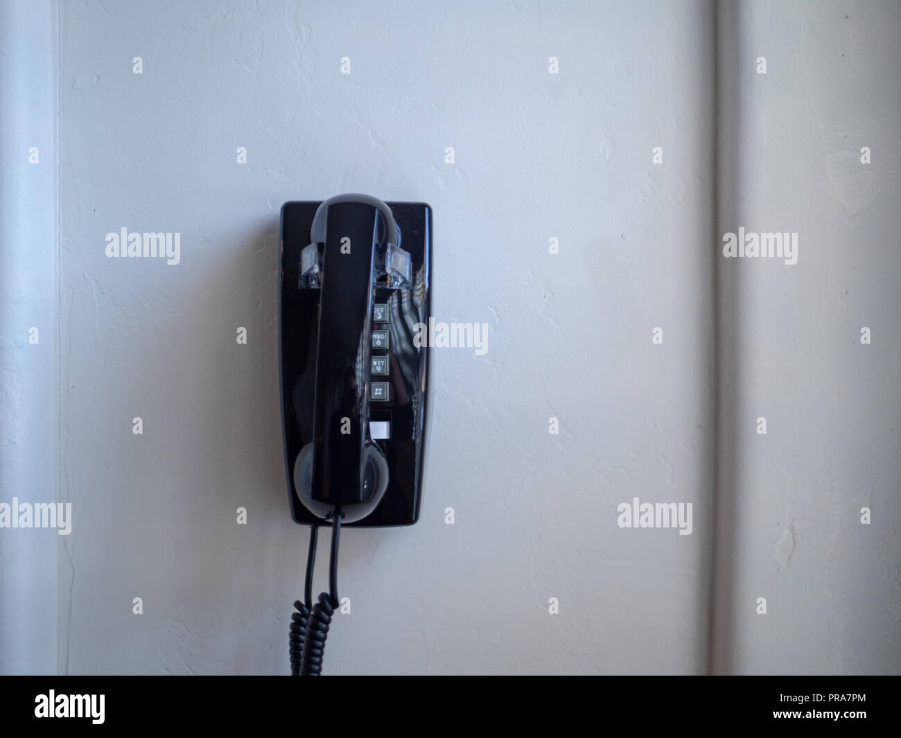 Teléfono fijo y receptor negro colgando en la pared blanca Foto de stock