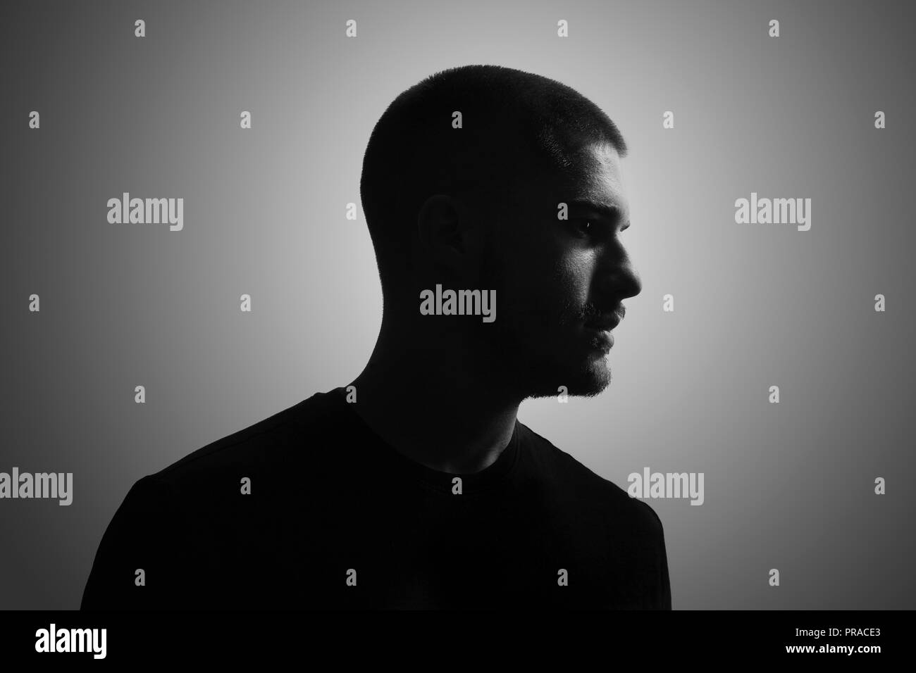 Blanco y negro, un hombre joven, 20-25 años, Moody retrato oscuro, perfil. Foto de estudio, fondo gris. cabeza y hombros shot. Foto de stock