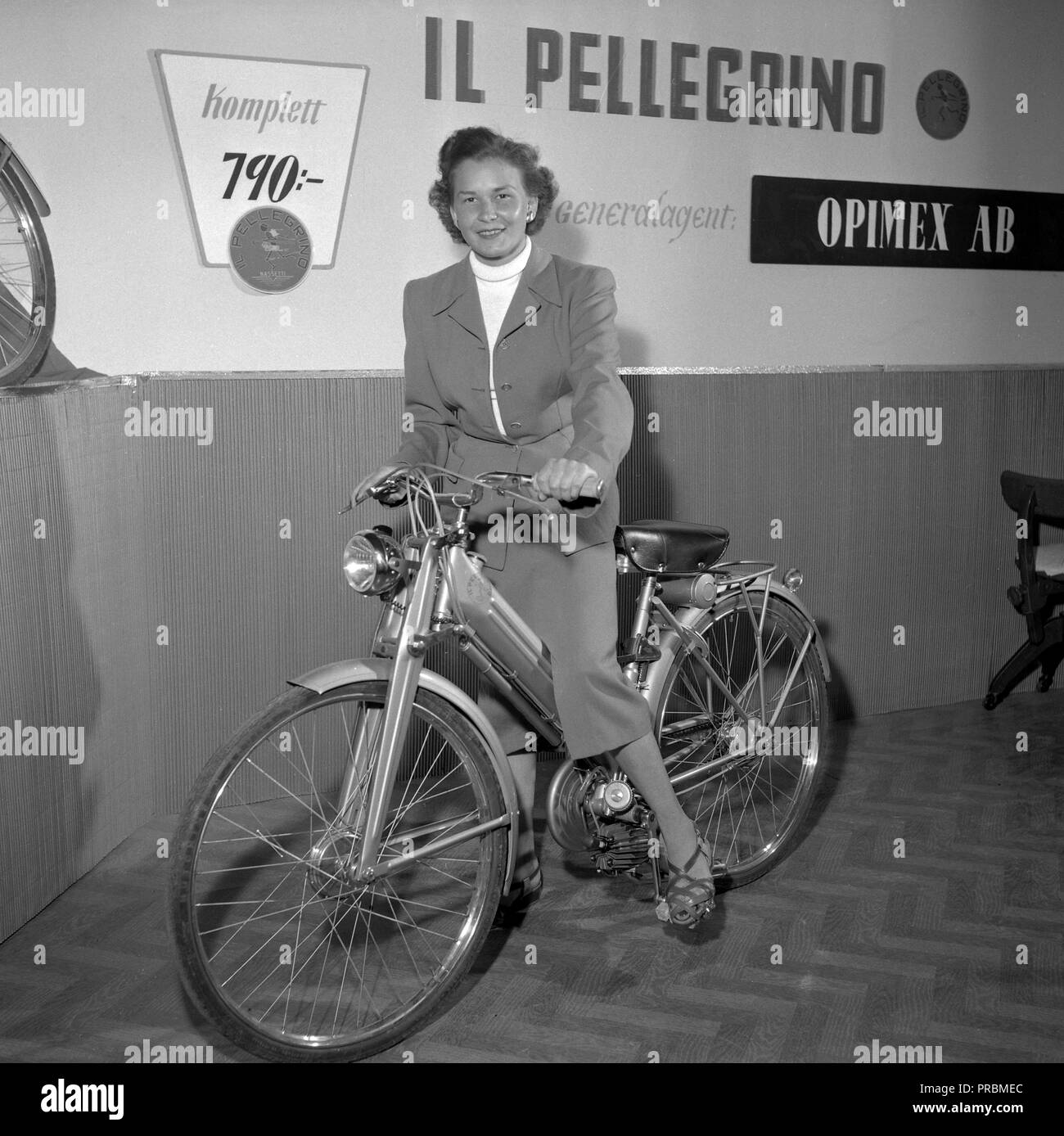 Un ciclomotor 1950 Bicicleta. Un modelo italiano retratado aquí en el lanzamiento del modelo en Suecia 1952 como Il Pellegrino y venta de 790 SEK. Una mujer joven está mostrando el ciclomotor en el St Eriks fair en Estocolmo en 1952. Datos técnicos: 48 cc motor montado en la parte posterior de rueda de bicicleta. Ref: 2110 Foto de stock