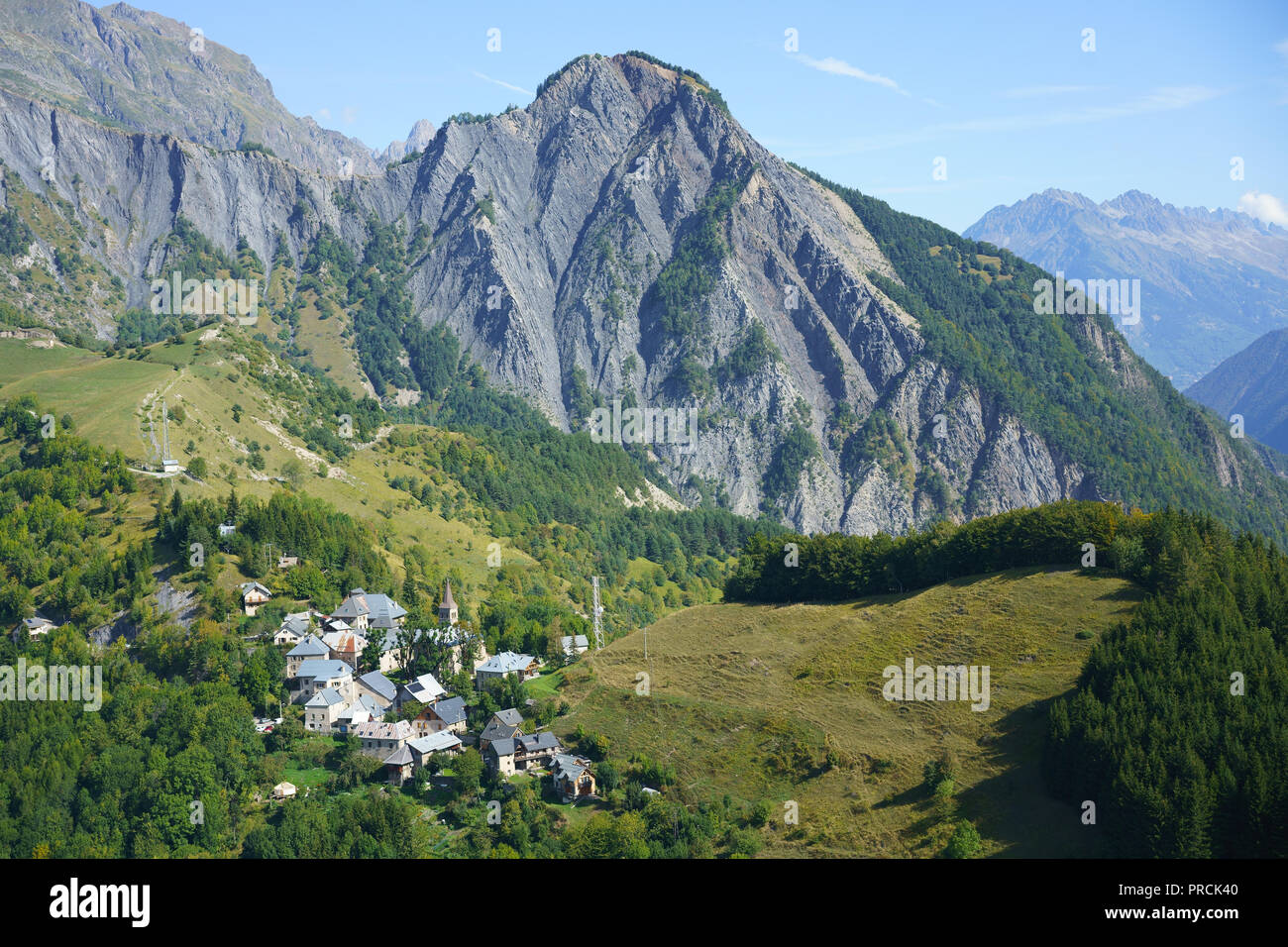 VISTA AÉREA. Pequeño pueblo con un paisaje montañoso escarpado para el fondo. Ornon, Isère, Auvernia-Rhône-Alpes, Francia. Foto de stock