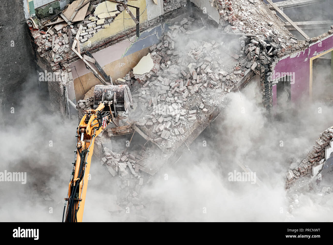 Demolición del edificio con una excavadora en nube de polvo, vista desde arriba. Foto de stock