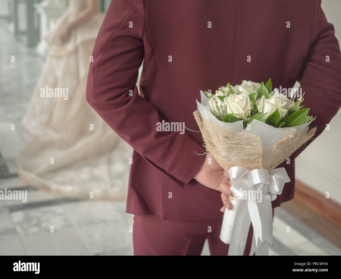 El novio en rojo borgoña o traje de novia ocultando bouquet blanco rosa  hermosa flor con cinta blanca detrás de su espalda con la novia Fotografía  de stock - Alamy