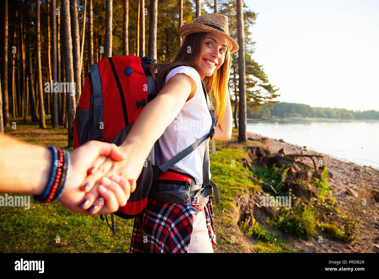 Retrato de mujer joven feliz sosteniendo la mano de su novio mientras caminaba en el bosque. Foto de stock