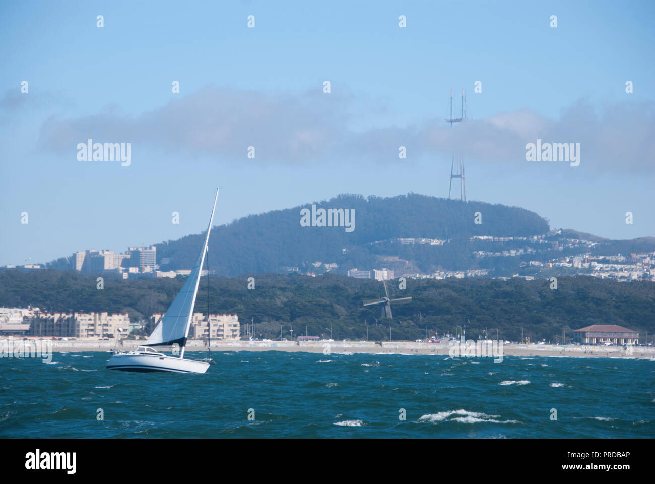 Un velero en el océano Pacífico frente a la costa de San Francisco con Sutro torre visible detrás de él. Foto de stock