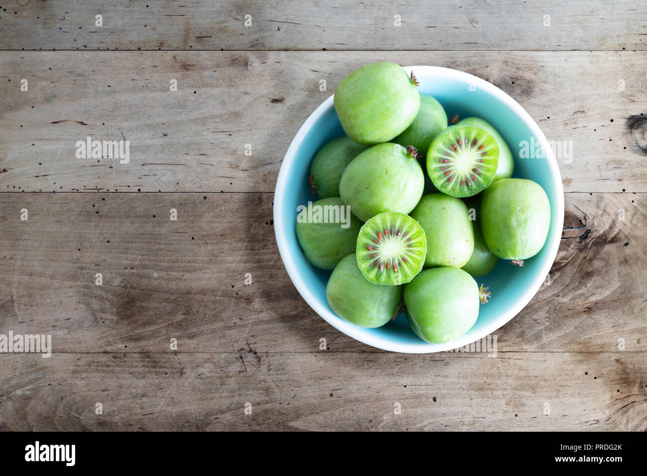 Frutos de kiwi hardy o kiwi bayas en cuenco de cerámica en la tabla Foto de stock