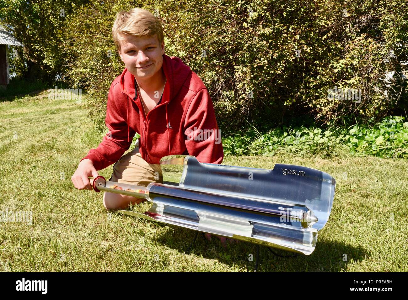 Niño varón adolescente cocinar una comida en un deporte GoSun sol solar  establecidos fuera del horno para cocinar, hornear asar alimentos  utilizando sólo el calor del sol. Ee.Uu Fotografía de stock -