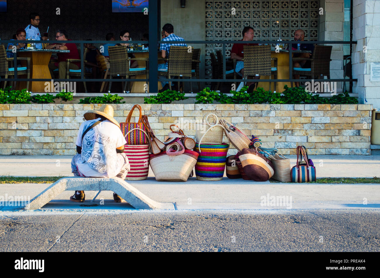 Vendedor callejero mexicano que vende maletas, esperando fuera de un restaurante caro. Ejemplo de desigualdad económica. Foto de stock