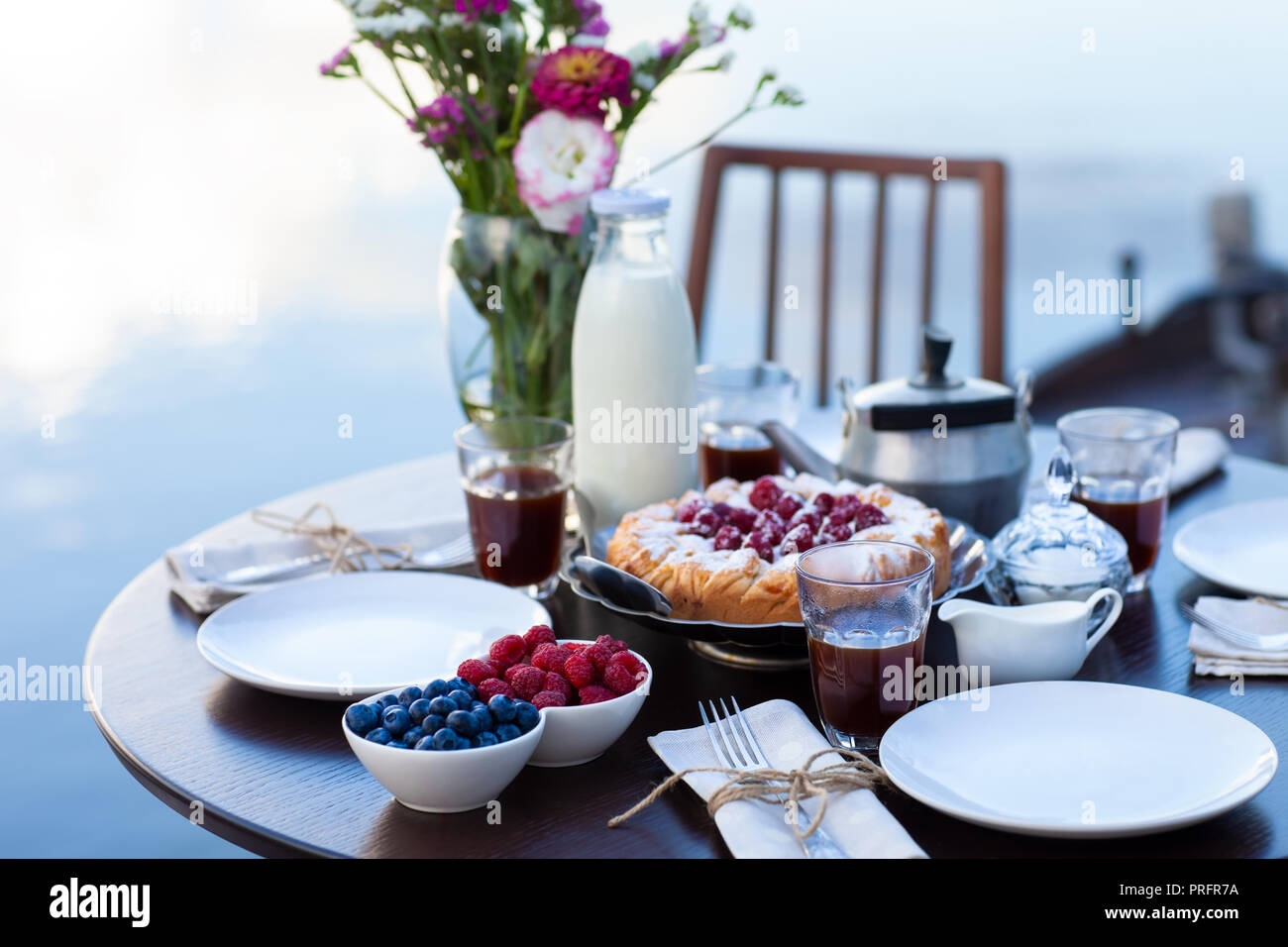 Cena romántica en la playa en el atardecer. Tarta casera y bayas. Tabla con alimentos, comida concepto Foto de stock