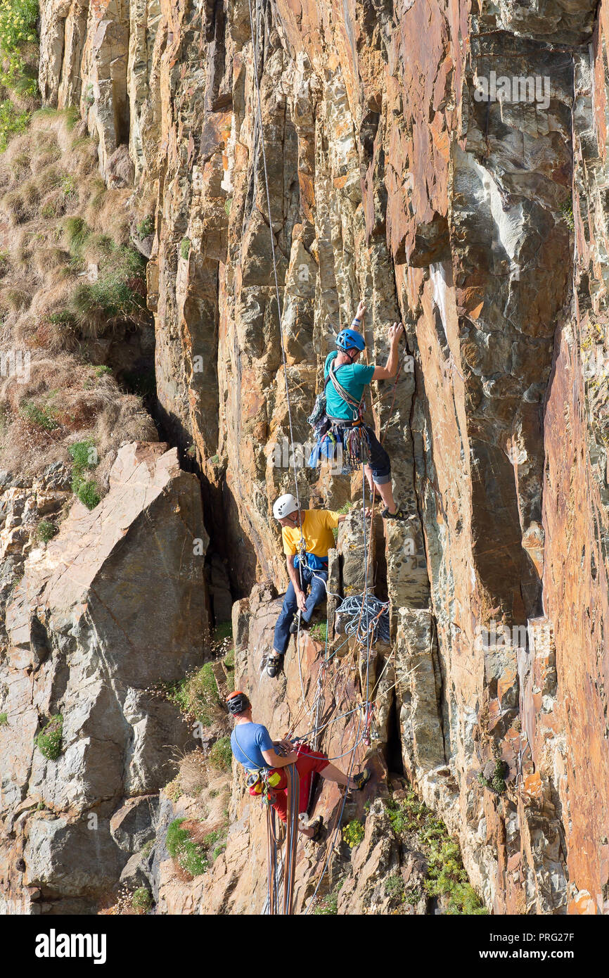 Capturar retratos, tres hombres disfrutando de desafío de extrema actividad deportiva: rappel y escalada en roca en rockface en South Stack Cliffs, Anglesey, Reino Unido. Foto de stock