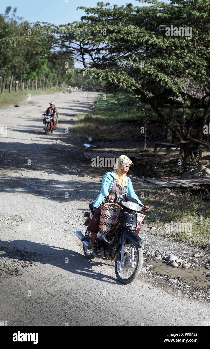 Mujer musulmana en moto por carretera rural en Sumbawa, Indonesia Foto de stock