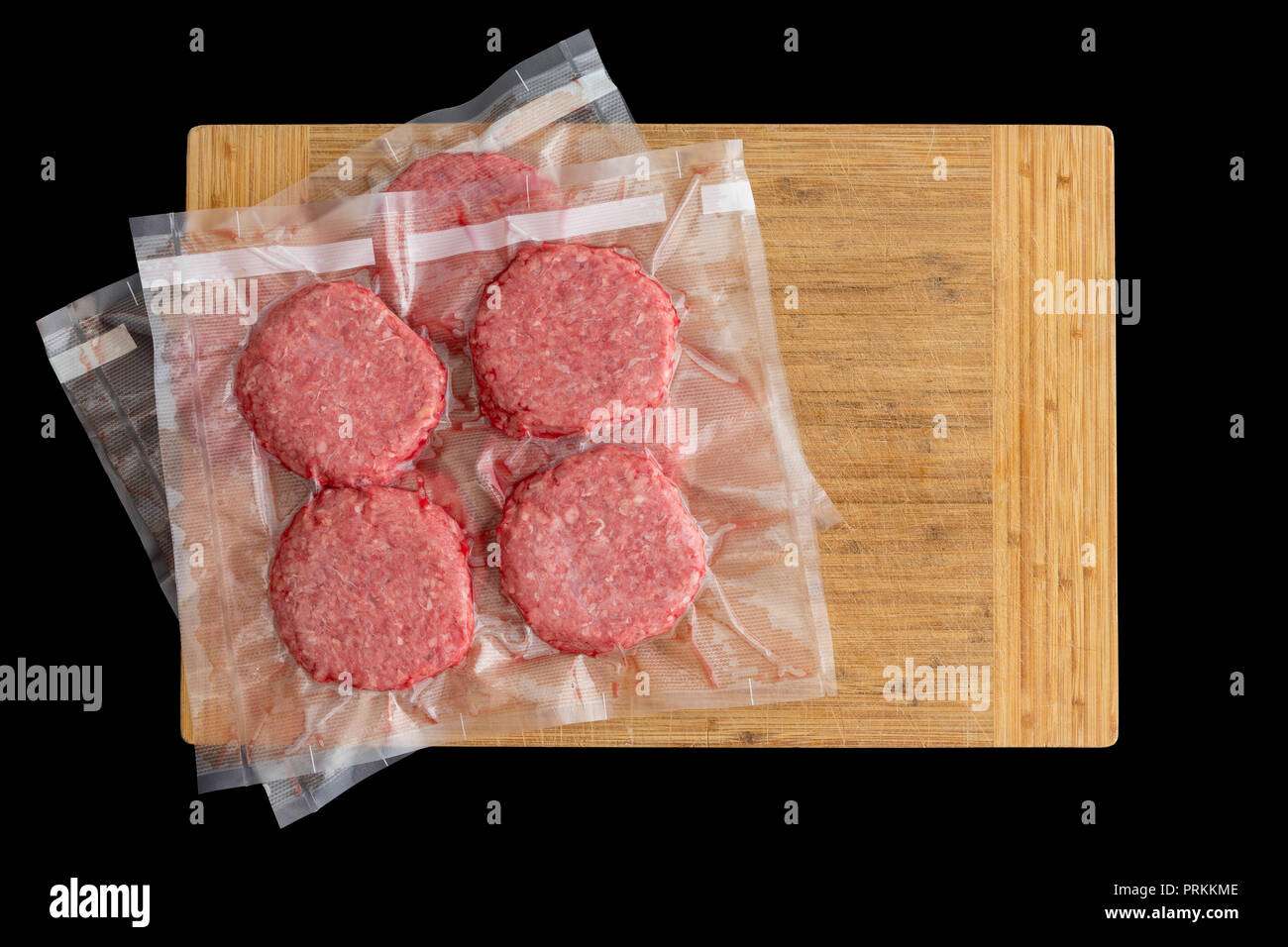 Hamburguesa de carne aislados empanadas preparado para congelar envasados  al vacío en plástico transparente listo para sous-vide cocinar en una vista  de arriba hacia abajo sobre una placa de madera en Fotografía