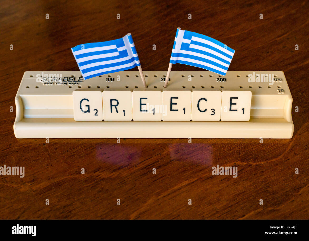 Scrabble letras de Grecia en el Scrabble bandeja con banderas griegas sobre fondo de caoba oscuro Foto de stock
