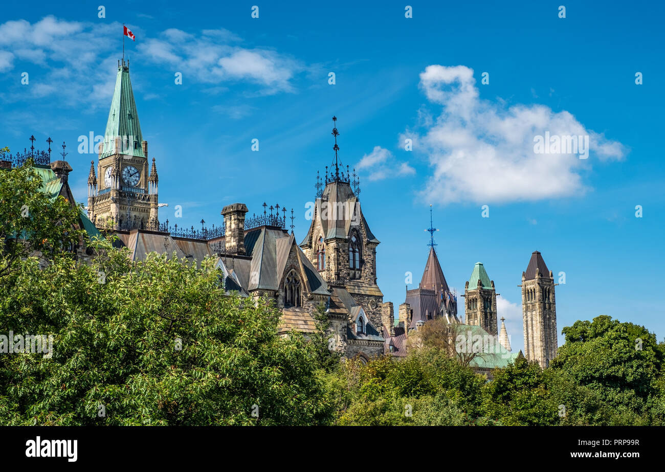 Una interesante vista lateral de los edificios del Parlamento canadiense, incluyendo la Torre de la paz por encima de los árboles emergentes con un hermoso cielo azul y blanco Foto de stock