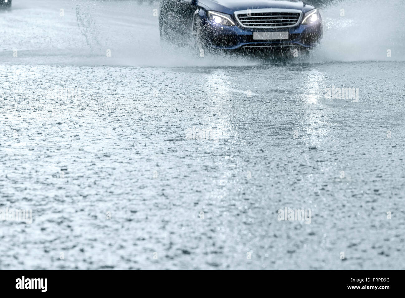 Coche en movimiento durante la lluvia pesada. Ciudad de asfalto camino cubierto con agua de lluvia Foto de stock