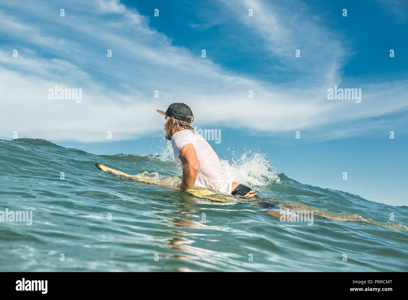 Vista lateral del surfista masculino natación sobre surfing junta en océano, en la playa de Nusa Dua, Bali, Indonesia Foto de stock