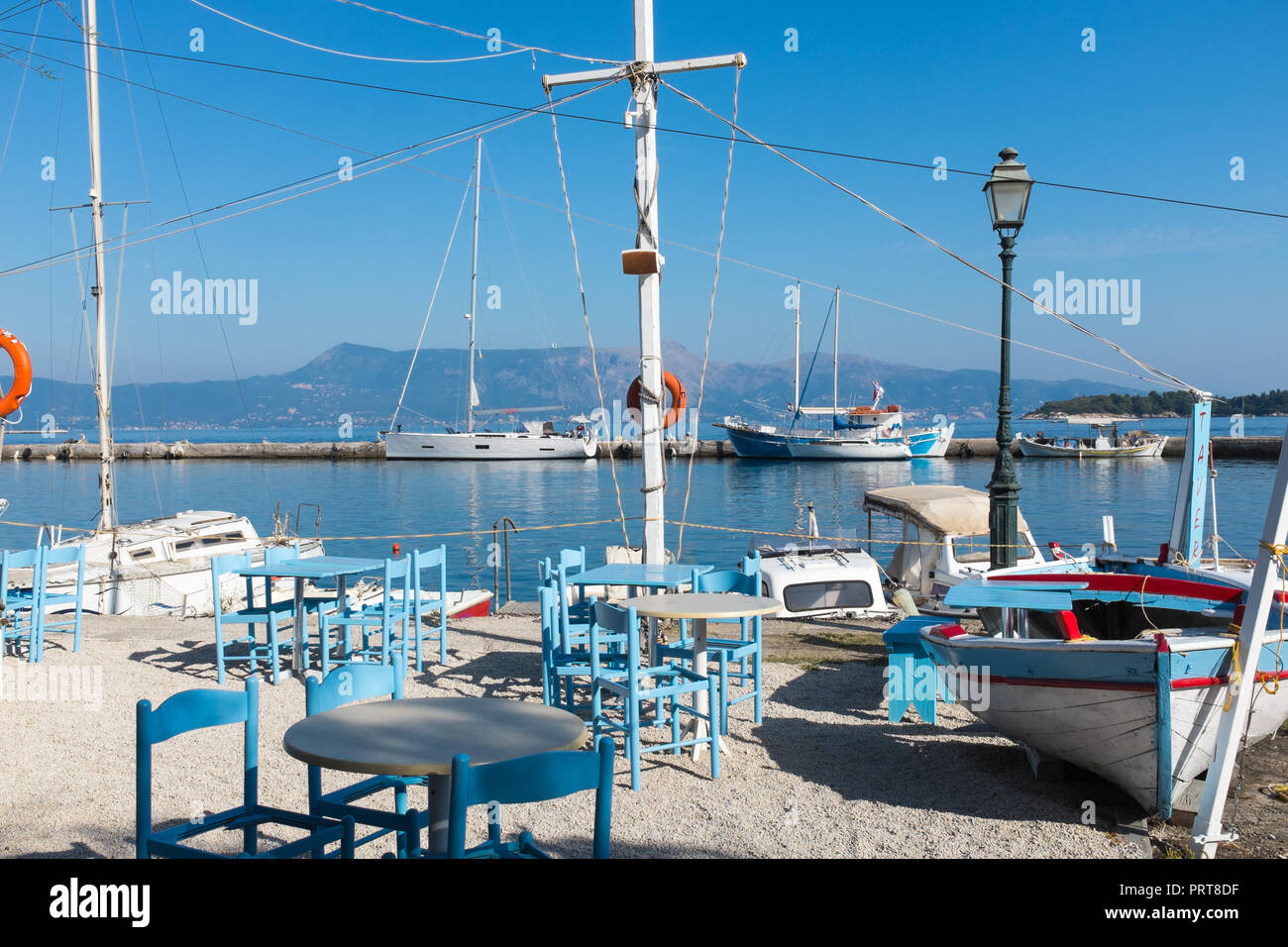 Taberna al aire libre por el puerto de Corfú con coloridas mesas y sillas  pintadas de azul y barco decorativo con signo Fotografía de stock - Alamy