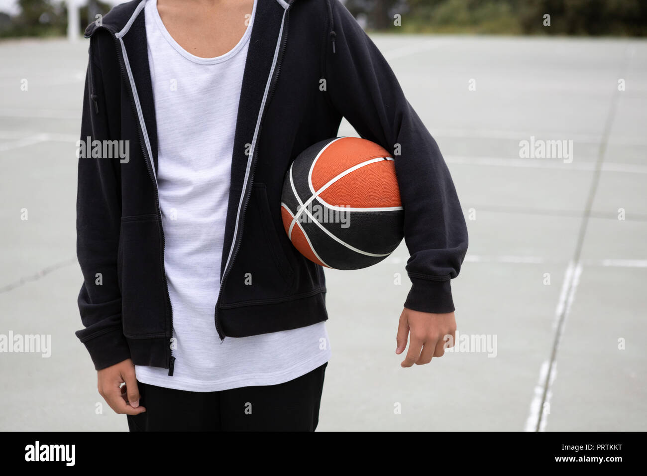 Adolescente masculino, jugador de baloncesto en la cancha de baloncesto con balón bajo el brazo, sección intermedia Foto de stock