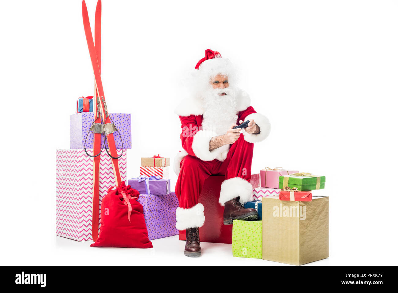 Santa Claus sentado sobre el montón de cajas de regalo jugar video juego por joystick aislado sobre fondo blanco. Foto de stock