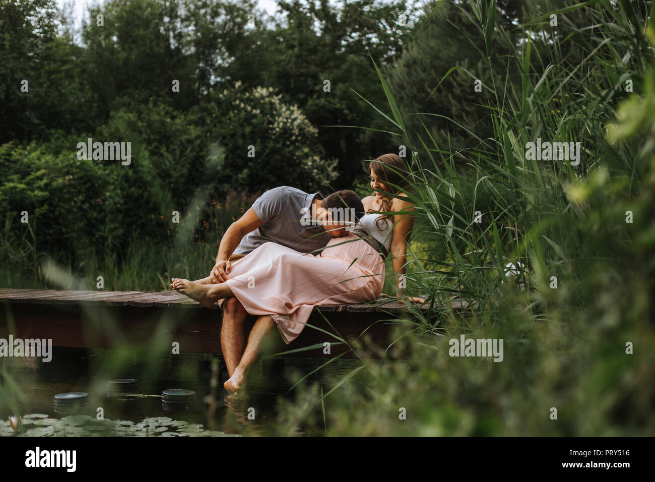 Marido besa a su esposa su vientre mientras se relaja en el lago Foto de stock