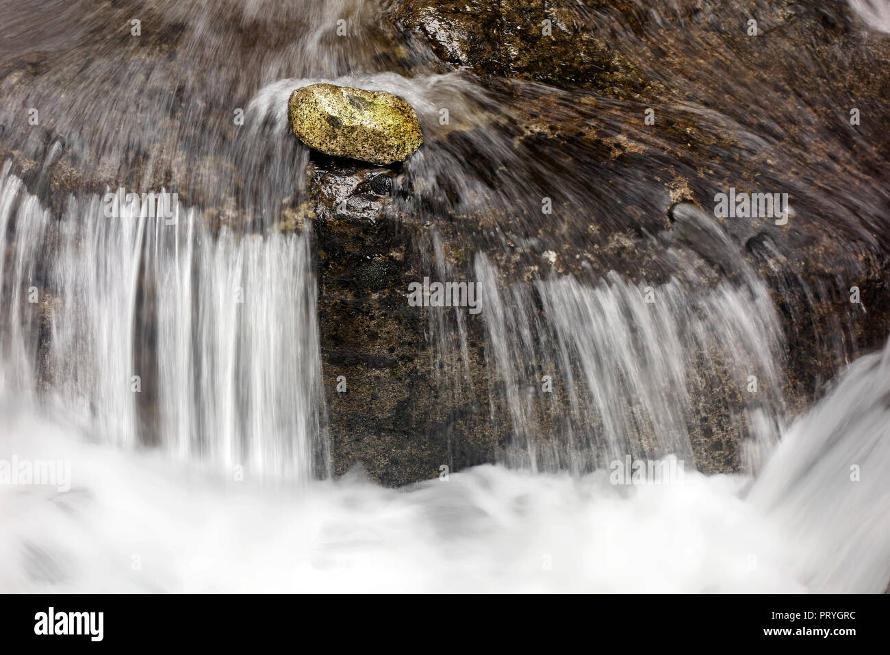 Stone se encuentra delante de una pequeña cascada de corriente, corriente de montaña, el simbolismo, la tenacidad, todos contra uno Foto de stock