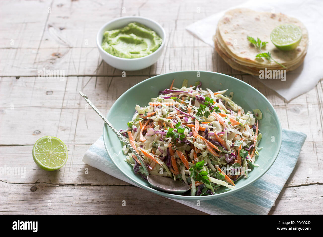 Coleslaw hechas de col, zanahorias y varias hierbas, servido con tortillas y guacamala sobre un fondo de madera. Foto de stock