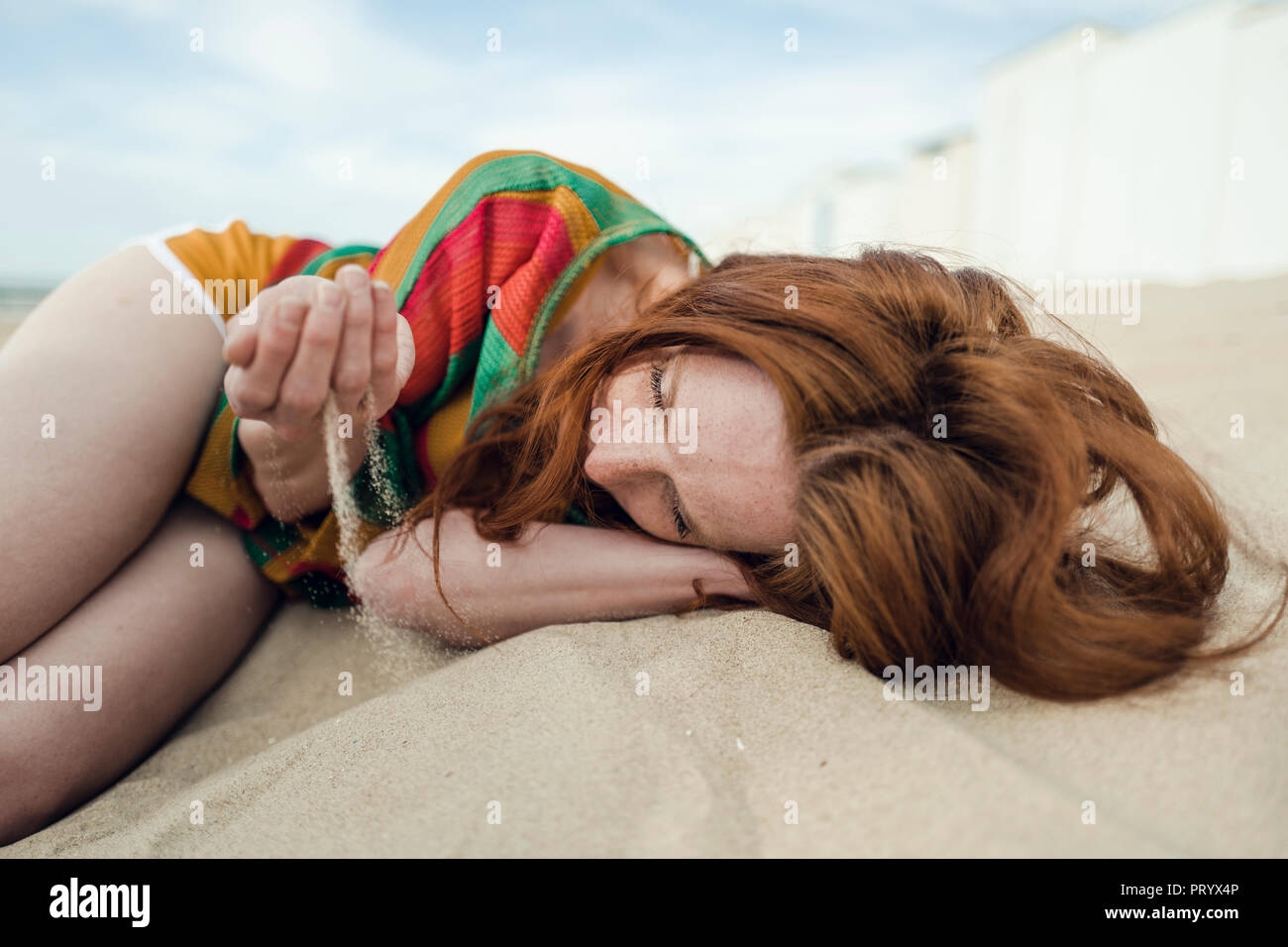 Pelirroja mujer acostado en la playa con arena goteando a través de su mano Foto de stock