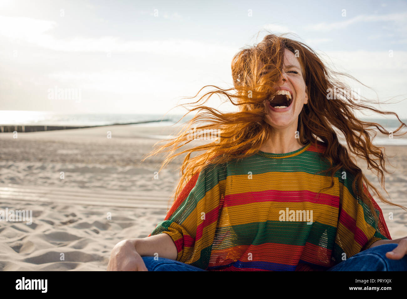 Mujer sentada en la playa, gritando de alegría Foto de stock