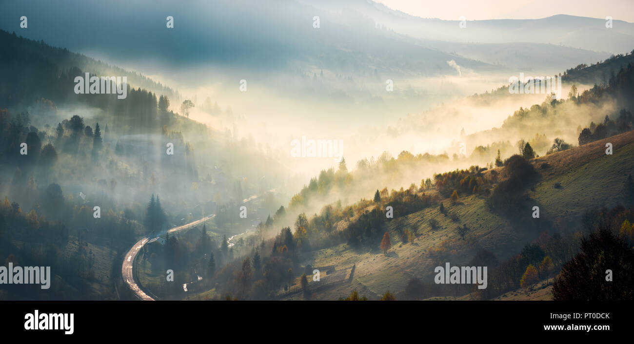 Panorama del increíble paisaje de las montañas al amanecer. brillante ascenso del bosque de niebla en colinas y caen en el valle. rayo de luz traza el haze en s Foto de stock