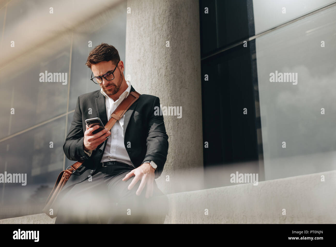 Hombre de negocios gestión de negocios en movimiento sentados al aire libre. Empresario sentado fuera de un edificio mirando su teléfono móvil. Foto de stock