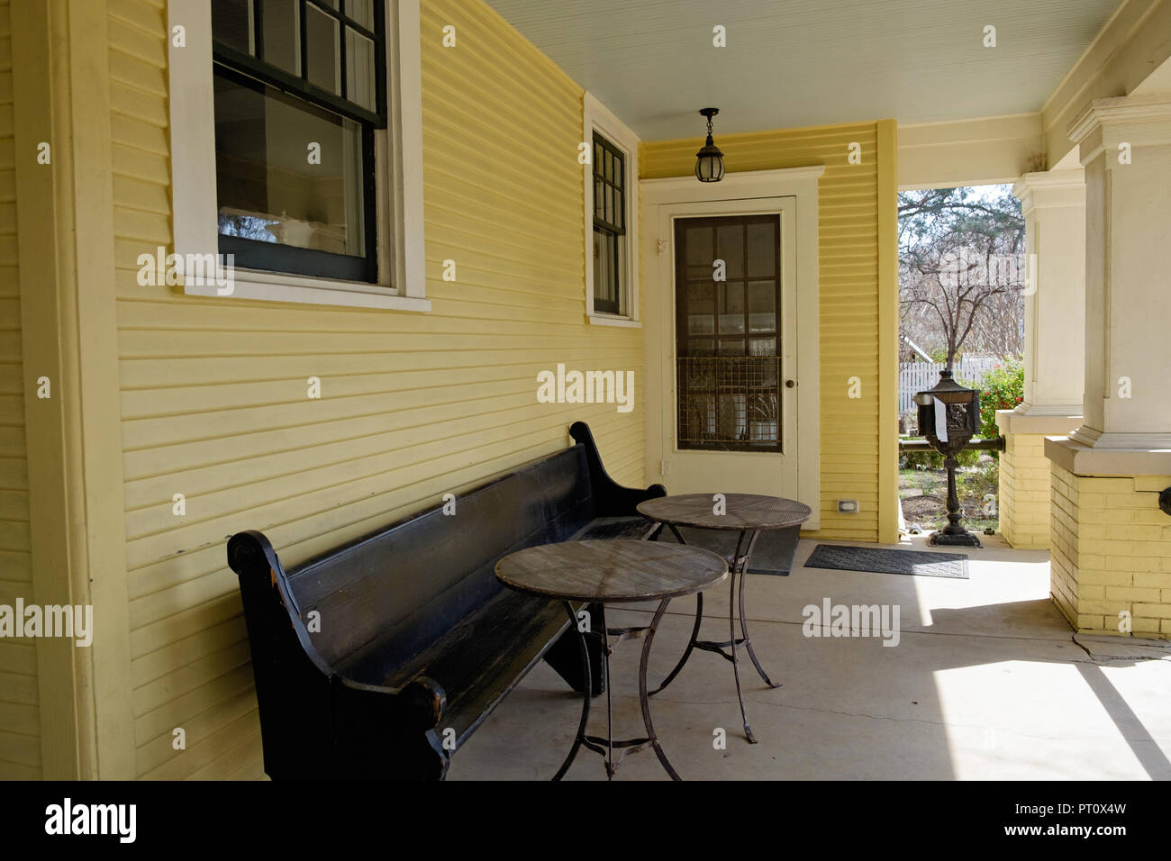 Casa histórica veransa, largo banco de madera y dos mesas redondas. Las tejas y ladrillos amarillos. Casa Dulaney Plaza Castaño Villa Histórica, McKinney, Texas. Foto de stock