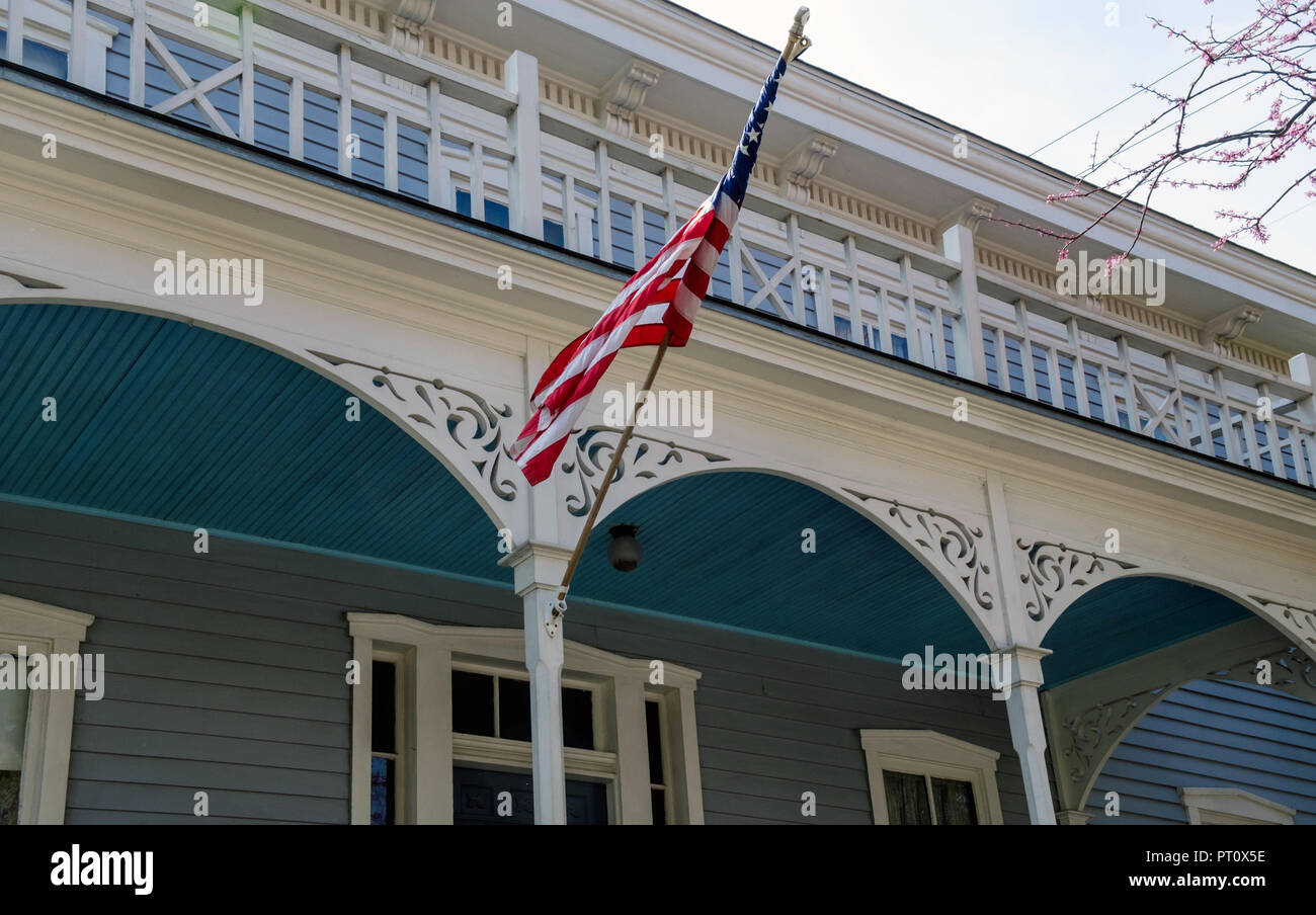 Bandera Americana extendido fuera de 2 pisos casa shingled azul con ribetes blancos. La casa de Johnson, Castaños Square Historic Village, McKinney, Texas. Foto de stock