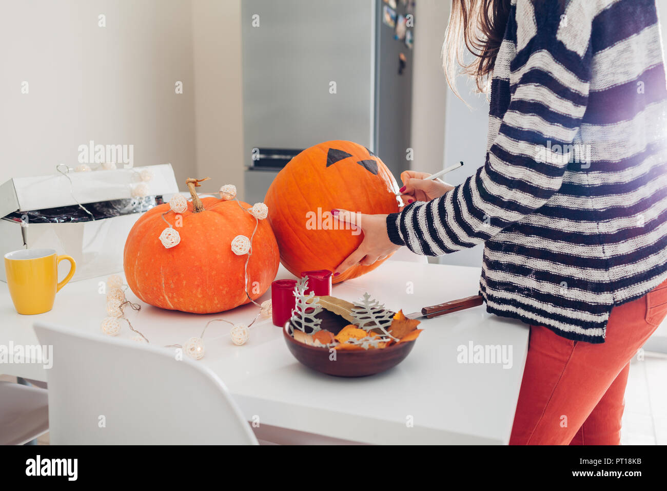Mujer joven haciendo jack-o-lantern para halloween en la cocina. Dibujar los ojos, la nariz y la boca con un lápiz sobre la calabaza. Preparar la decoración para vacaciones Fotografía de stock - Mujer joven haciendo jack-o-lantern para halloween en la cocina. Dibujar los ojos, la nariz y la boca con un lápiz sobre la calabaza. Preparar la decoración para vacaciones Fotografía de stock -