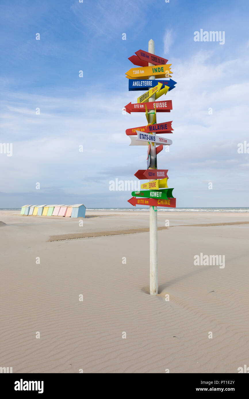 Cartel con las direcciones a ubicaciones internacionales en la playa de Berck-Plage, Francia, coloridas cabañas de playa en el fondo. Foto de stock