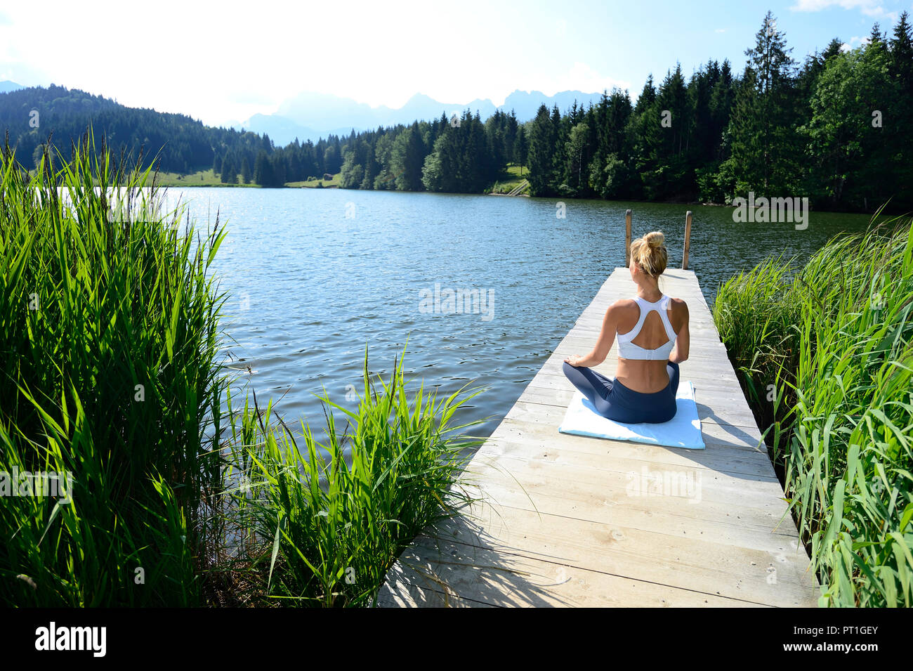Alemania, Mittenwald, vista posterior de la mujer practicando yoga en el embarcadero del lago Foto de stock