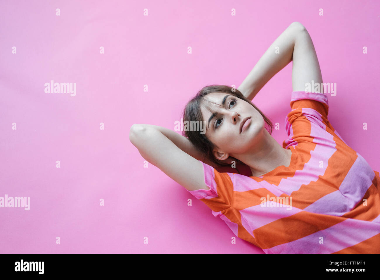 Mujer recostada sobre fondo de color rosa con las manos detrás de la cabeza, el pensamiento Foto de stock