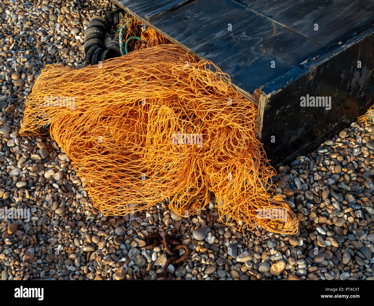 Red de pesca naranja Nylon saliendo de una caja de madera negra en una playa de guijarros Foto de stock