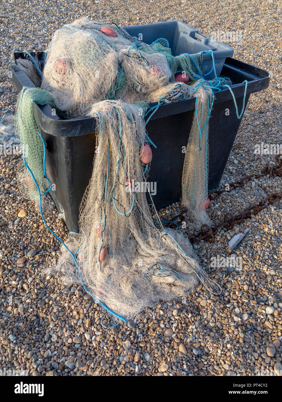 Redes de pesca de nylon saliendo de un contenedor de plástico gris sobre una playa de guijarros Foto de stock