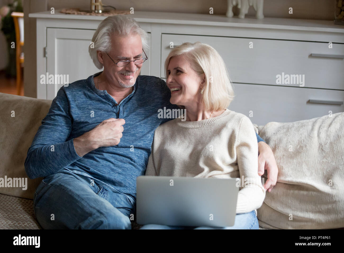 Feliz pareja de mediana edad senior riendo relajante con portátil en el salón, los ancianos mature familia disfrutando online divertido humor sonriendo divirtiéndose Foto de stock