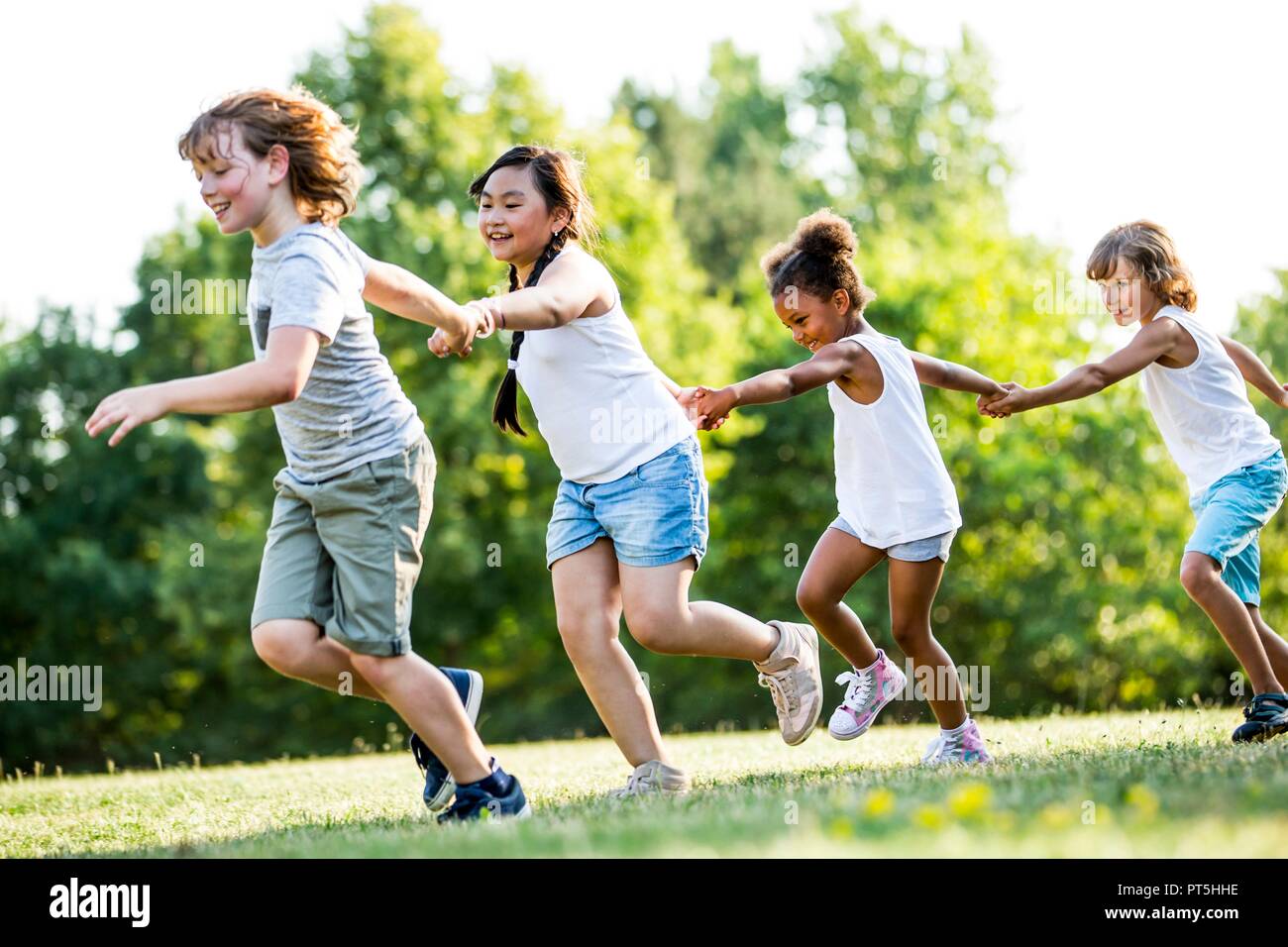 Los niños tomados de las manos y corriendo en el parque, sonriendo. Foto de stock