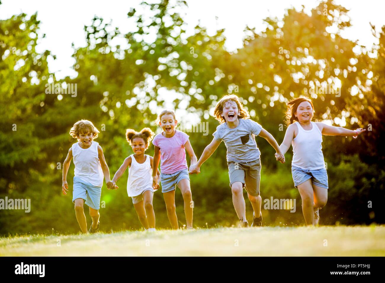 Los niños tomados de las manos y corriendo en el parque, riendo. Foto de stock
