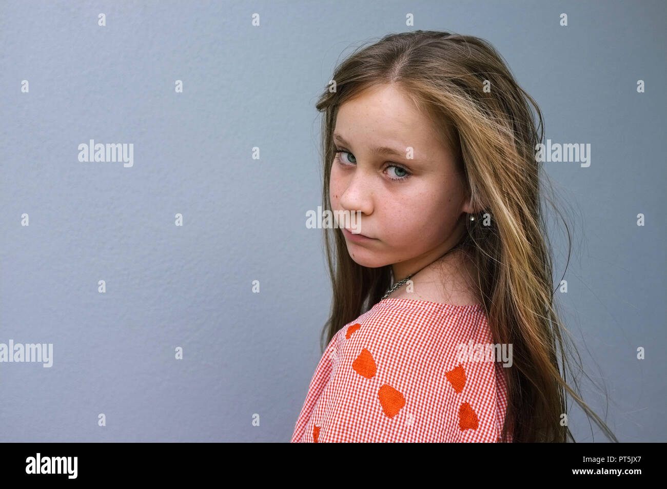 Retrato de una niña pre-adolescentes mirando por encima del hombro, contra una pared gris. Foto de stock