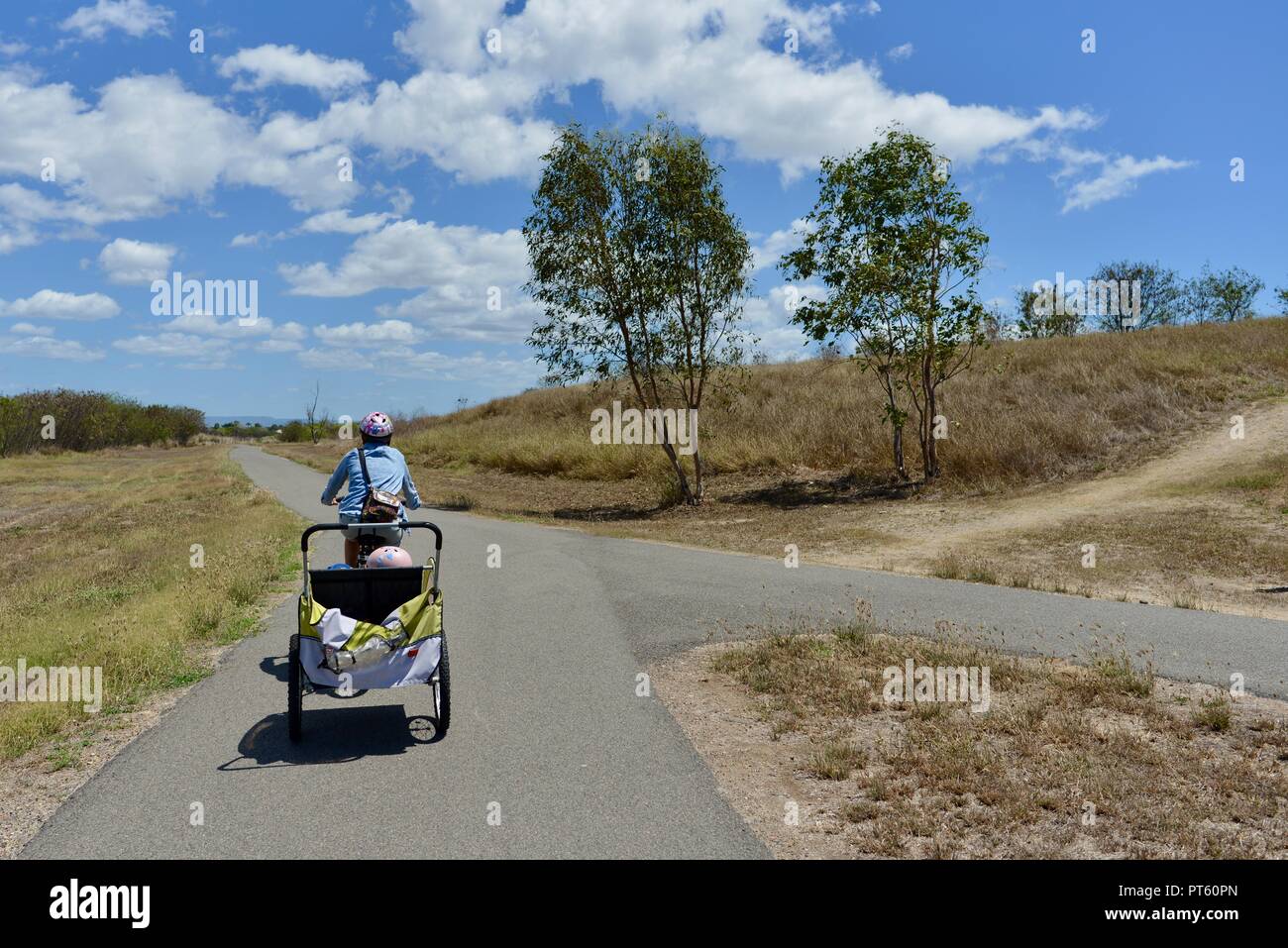 Mujer en bicicleta con un remolque de bicicleta para niños, Townsville, Queensland, Australia Foto de stock