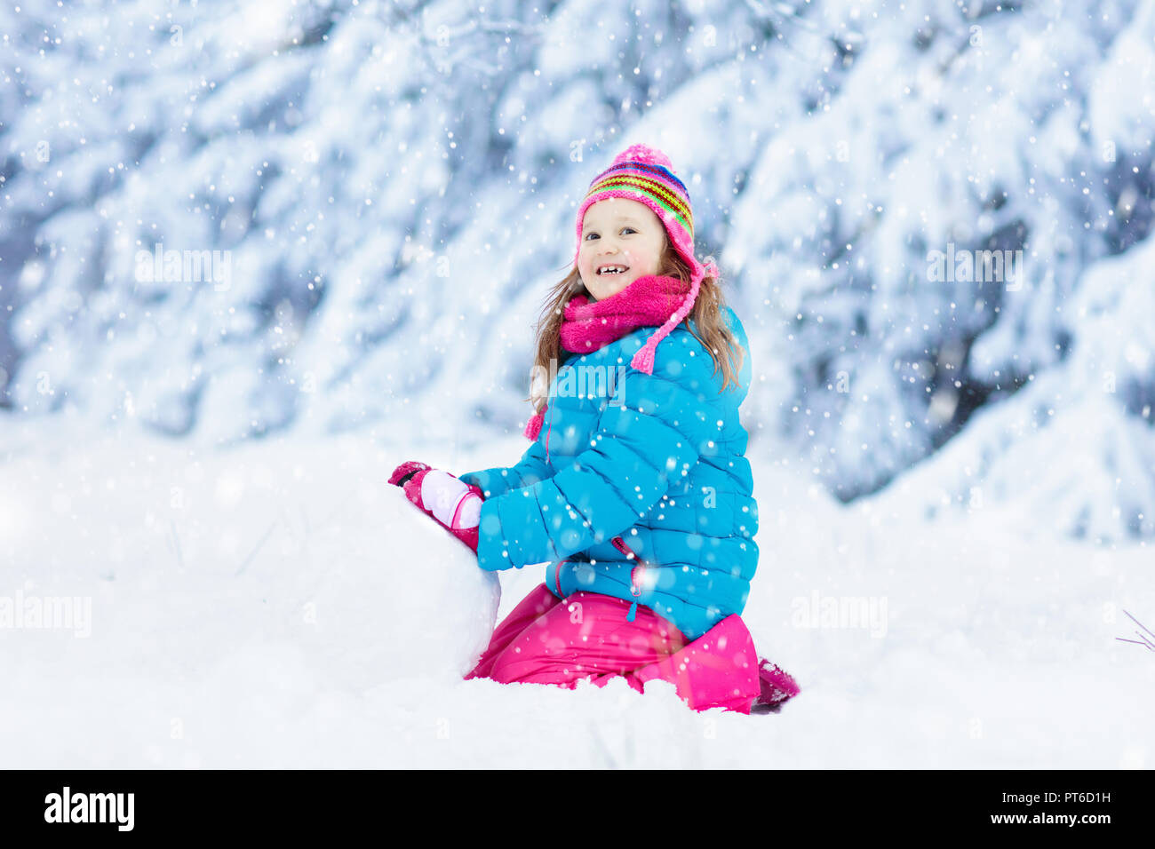 Kid haciendo el muñeco de nieve en parque de nieve del invierno. Los niños juegan en la nieve. Niña en un colorido edificio de chaqueta y sombrero de hombre de nieve