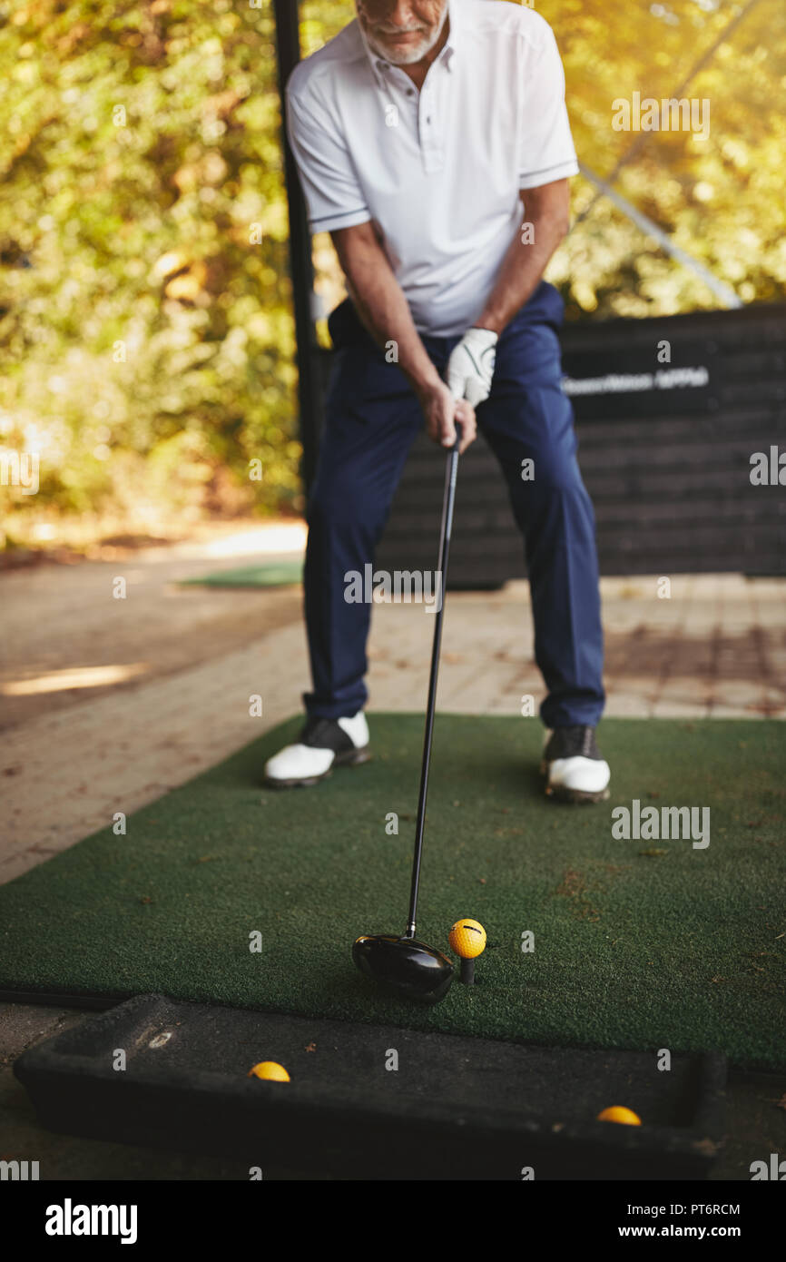 Senior deportivo hombre permanente fuera de practicar su swing de golf en un driving range en un día soleado Foto de stock