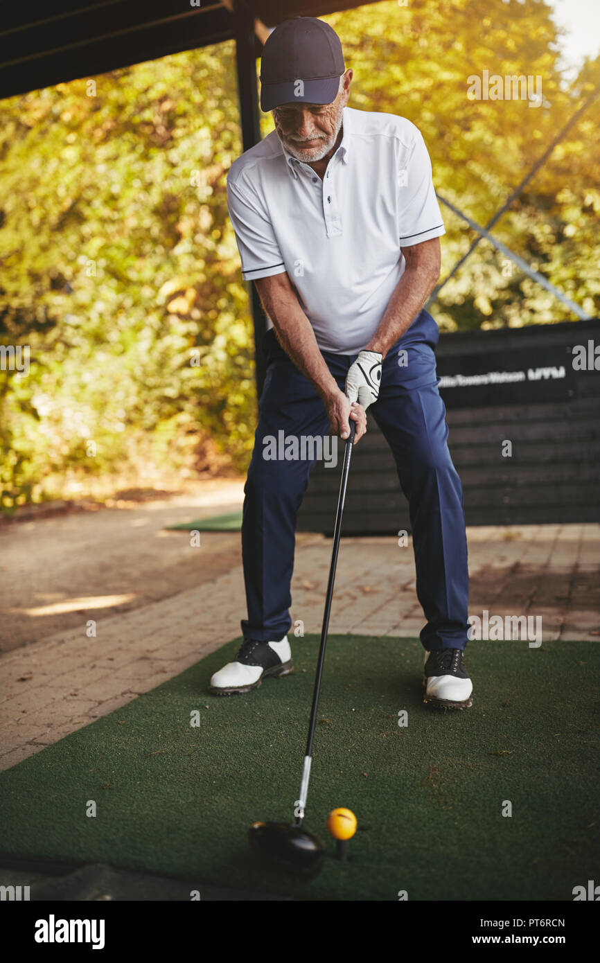 Senior deportivo hombre de pie sobre un driving range de golf practicar su swing en un día soleado Foto de stock